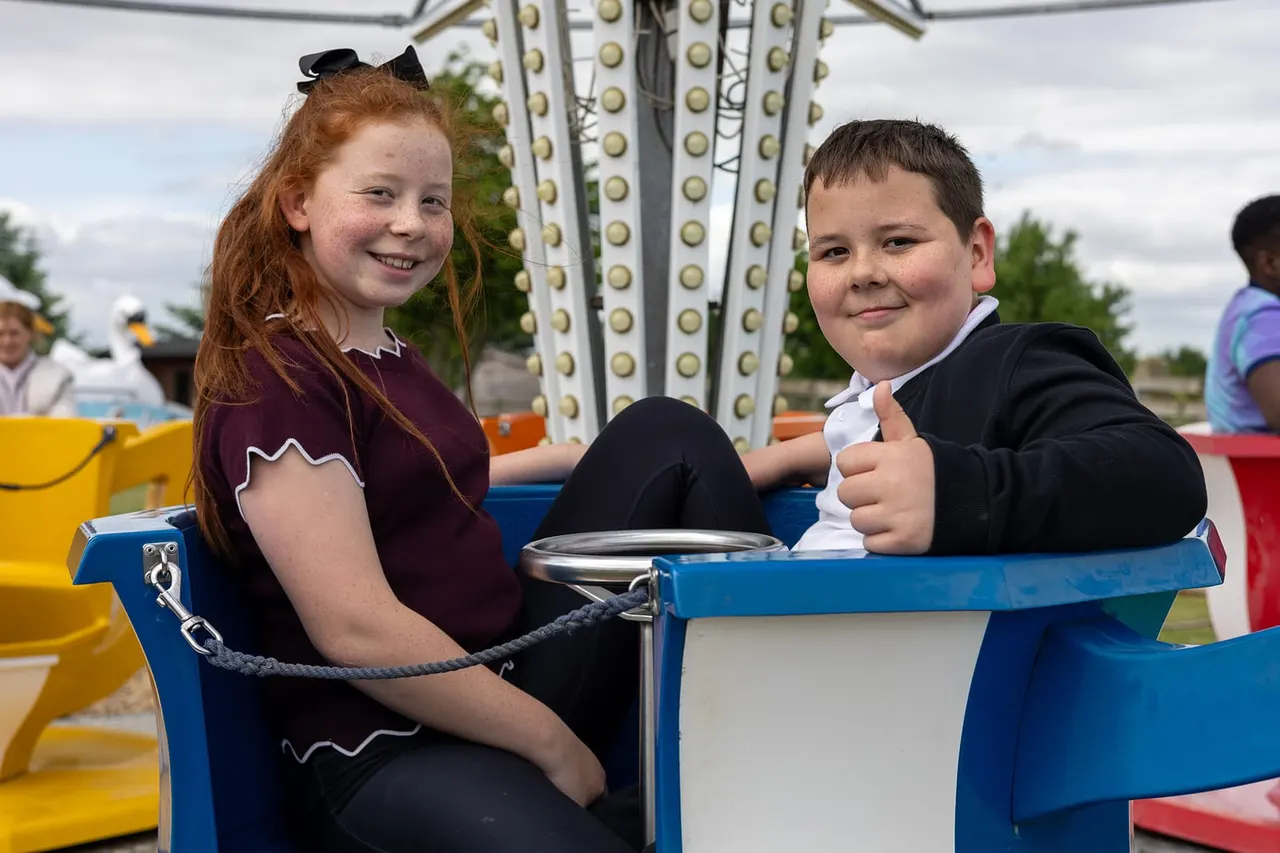 Two children riding together in a blue fairground ride car with metal framework above.