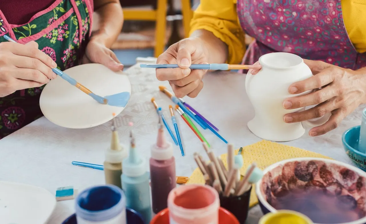 Children painting white ceramic bowls with brushes and colourful paints at a craft activity table.
