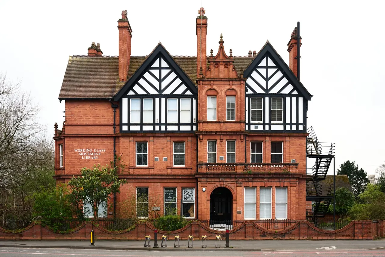 Victorian red brick building with black and white half-timbered gables, ornate chimneys, and multiple storeys fronting a street.