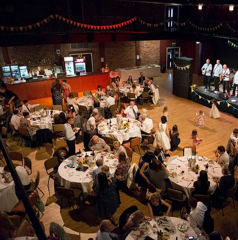 Guests seated at round tables during a formal dinner event in a brick-walled venue decorated with bunting.