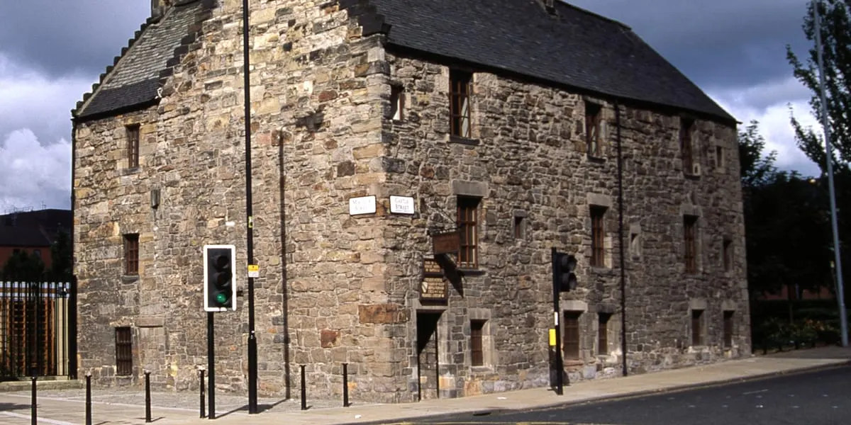 Historic stone building with multiple storeys and dark slate roof, situated on an urban street corner.