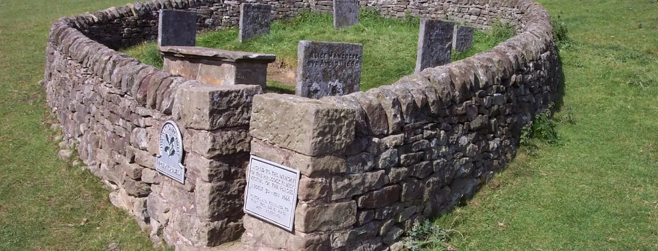 Ancient stone ruins with plaques and gravestones on grass, showing archaeological remains of a historical settlement.