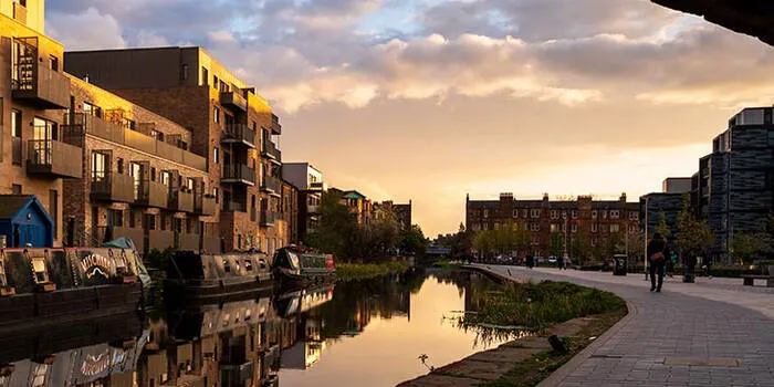 Canal waterway with moored boats, historic brick buildings reflected in still water at sunset.