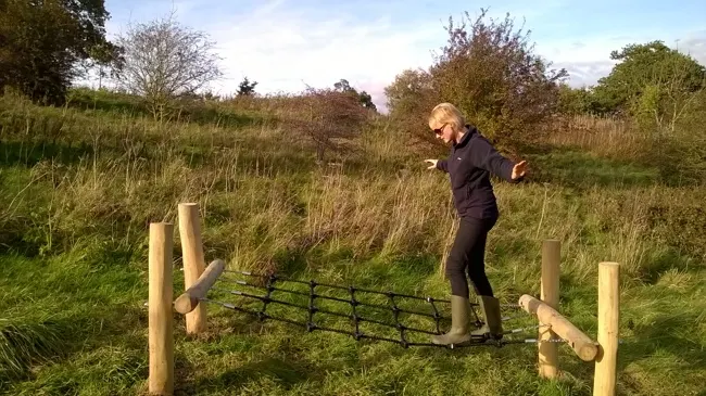 Person jumping over a wooden and metal fence obstacle in an open grassy field.