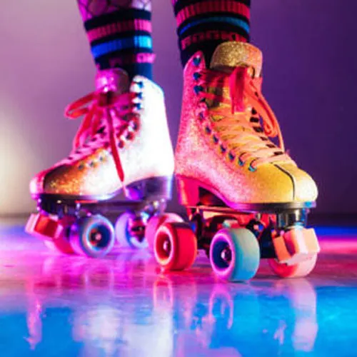 Pair of roller skates with illuminated wheels and glitter finish, worn with striped socks, against a purple and blue neon backdrop.