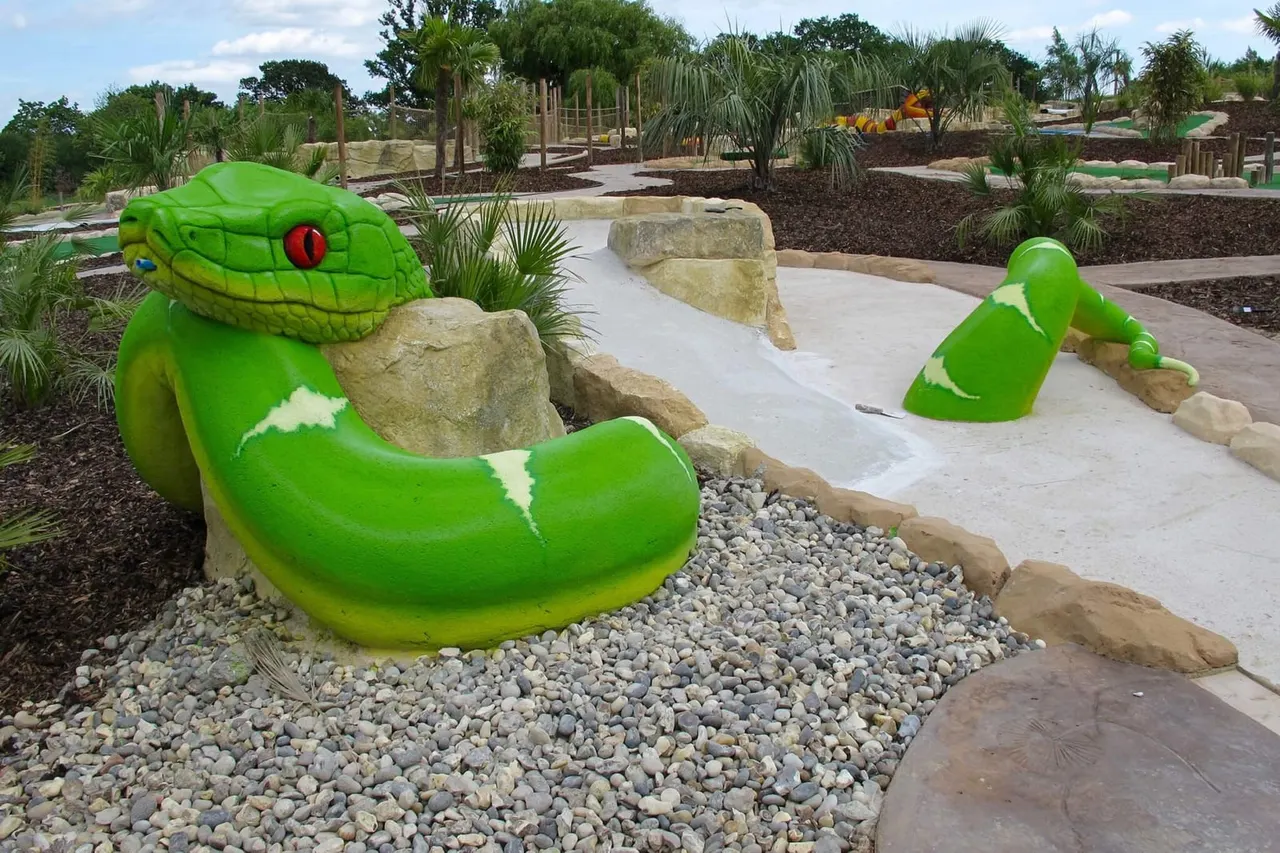 Bright green serpent-shaped mini golf obstacles on a tropical-themed course with palm trees and stone features in the background.