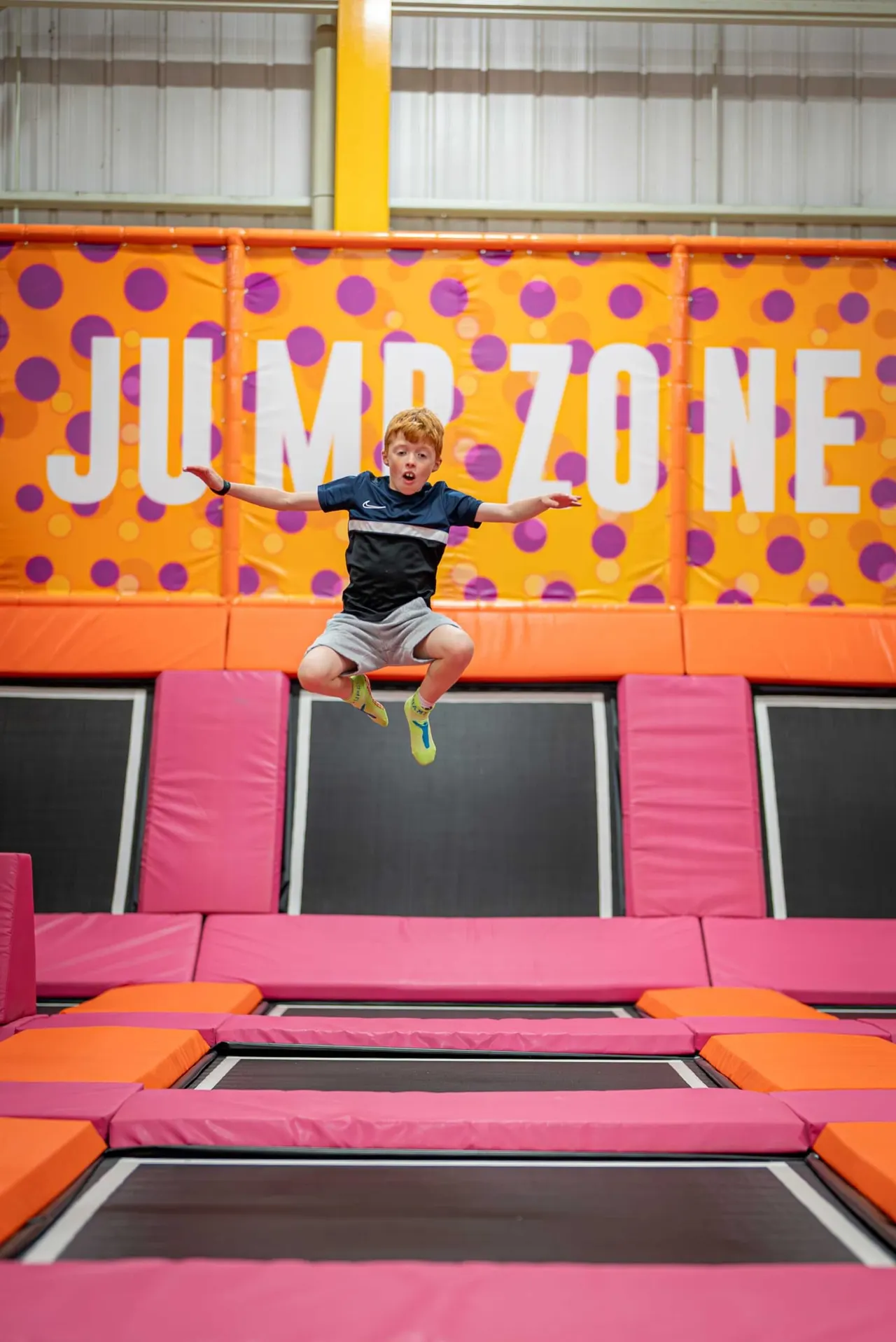 Child jumping on a trampoline with arms outstretched at an indoor jumping venue.