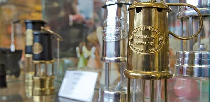 Close-up of vintage brass and metal safety lamps displayed in a museum exhibition about coal mining heritage.