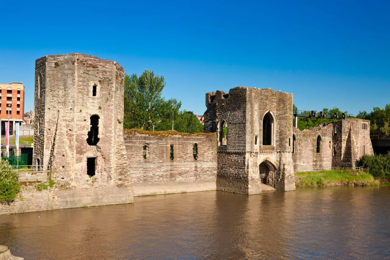 Ruins of a medieval fortified structure with stone towers and walls partially submerged in a river under clear blue sky.