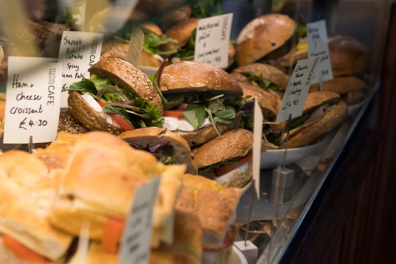 Array of fresh sandwiches and filled rolls on display with individual price labels in a café counter.