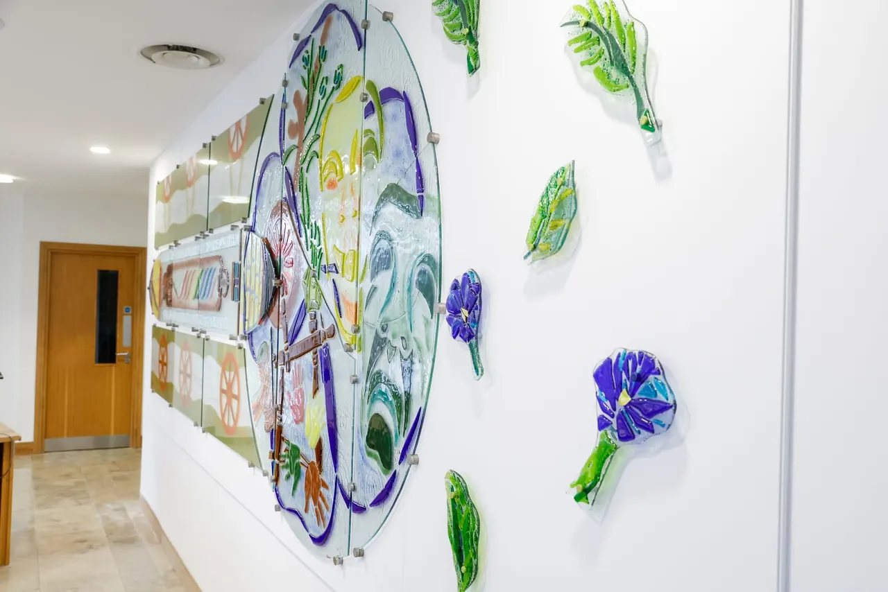 Indoor gallery corridor displaying hand-painted botanical artwork on white walls, including purple flowers and green foliage illustrations.