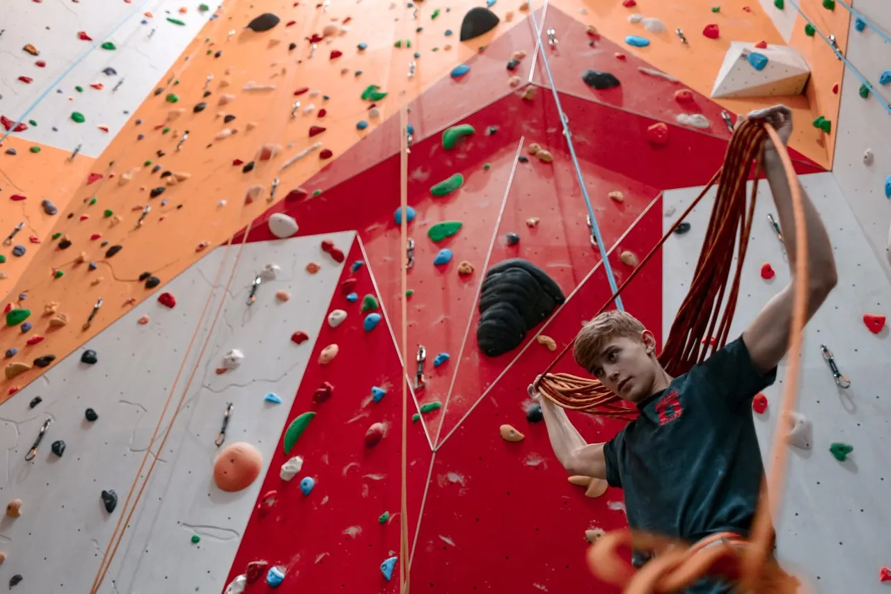 Young person rock climbing on an indoor climbing wall with coloured hand and foot holds.
