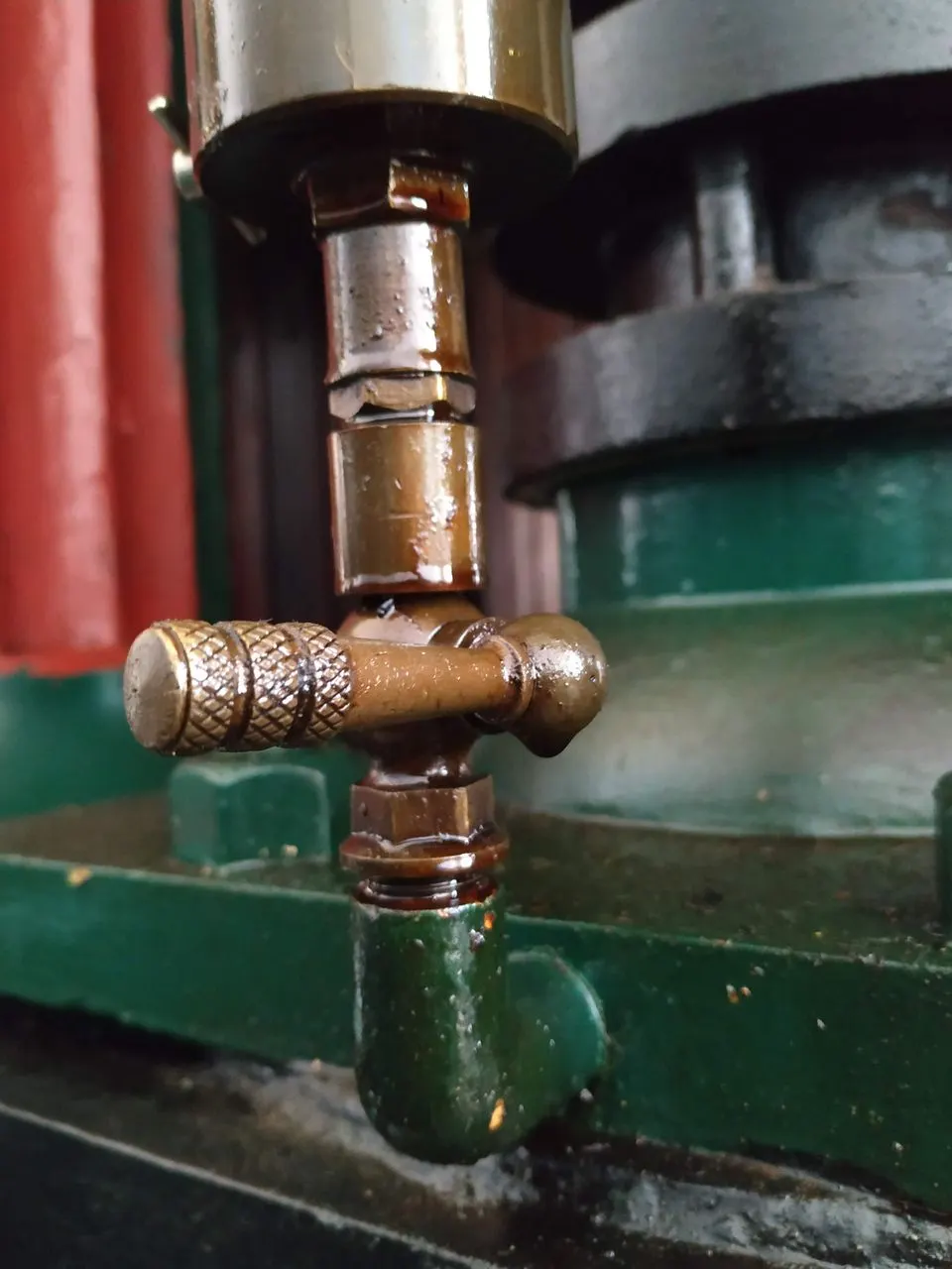 Close-up of an ornate brass tap valve on vintage industrial machinery with green and red painted metalwork.