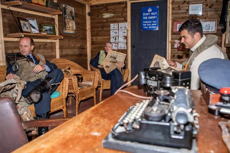 Three men in a wood-panelled Second World War museum room examining vintage radio equipment and memorabilia.