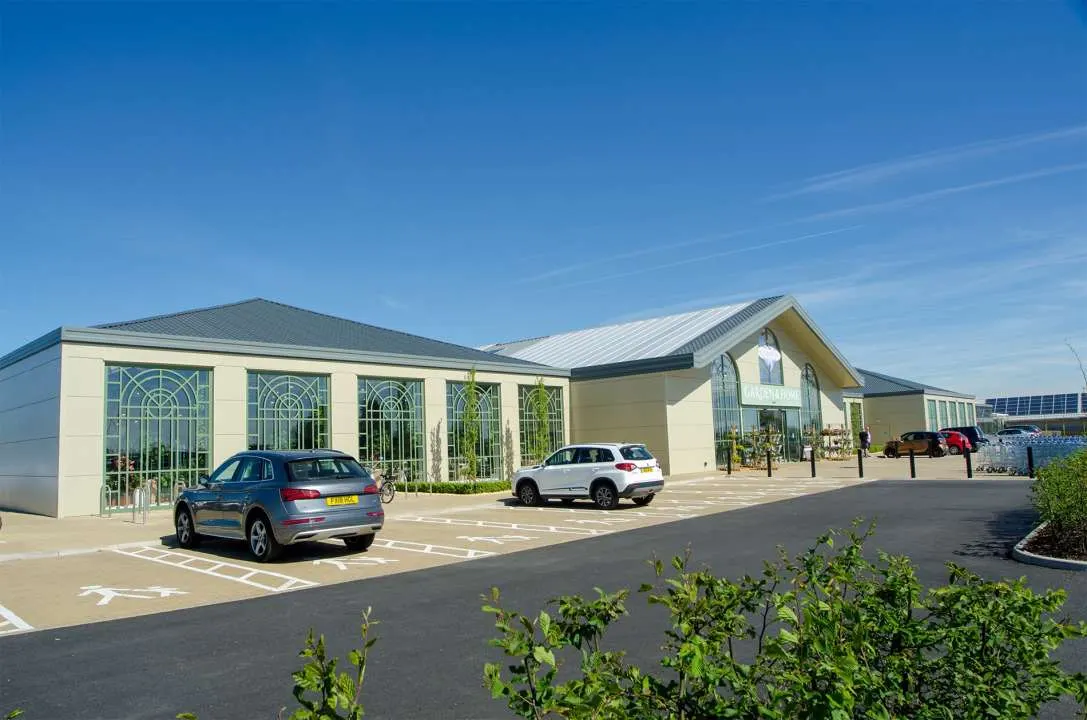 Modern leisure venue building with cream and grey exterior, parked cars in foreground, clear blue sky.