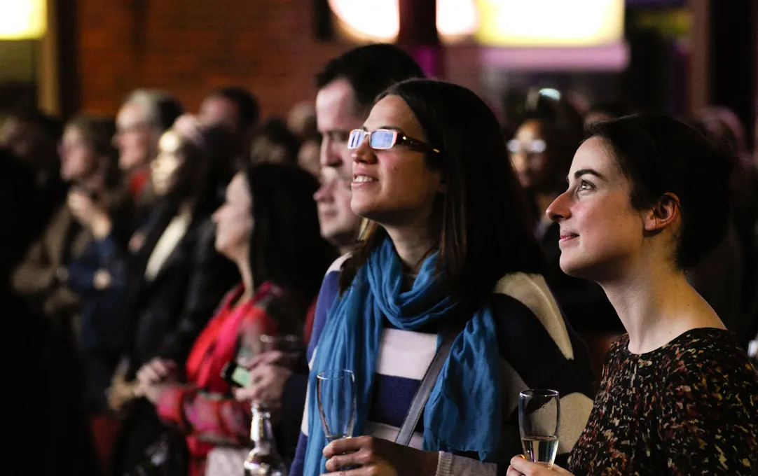 Audience members wearing 3D glasses watch a film screening in a cinema, holding drinks.