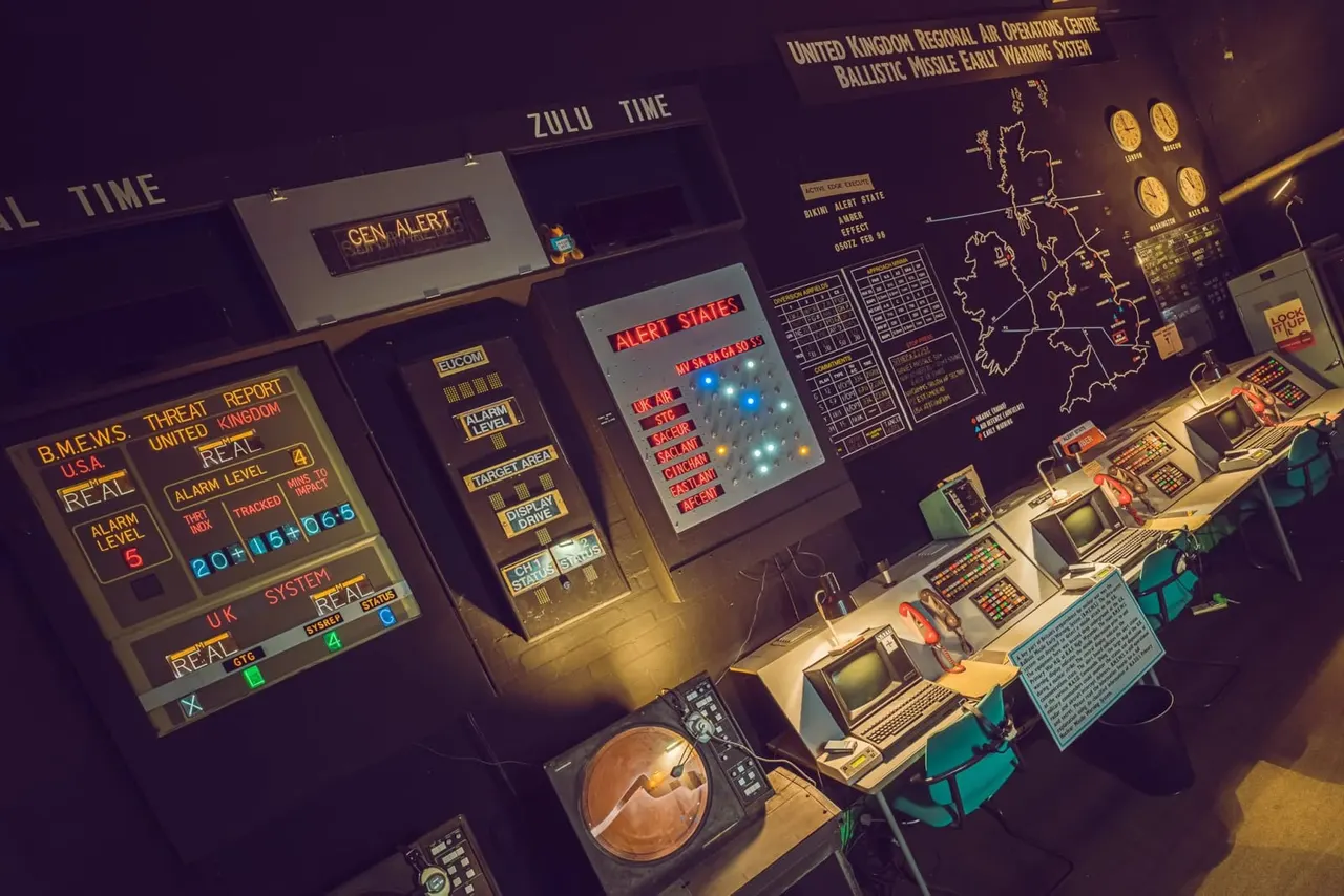 Historic military operations control room with illuminated display panels, radar screens, alert systems and vintage computer equipment from the Cold War era.