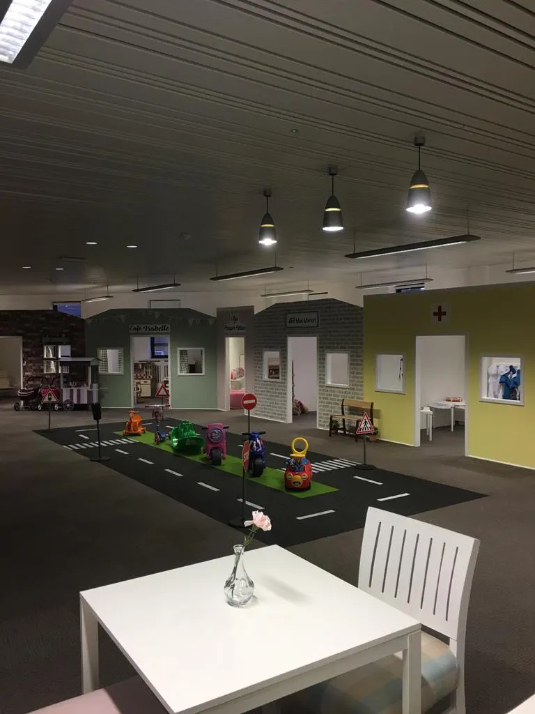 Indoor play area with toy vehicles on a road-themed mat and themed activity pods with coloured walls.
