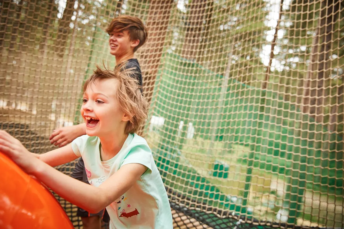 Two children laughing whilst navigating a rope and net obstacle course inside a canopy structure.