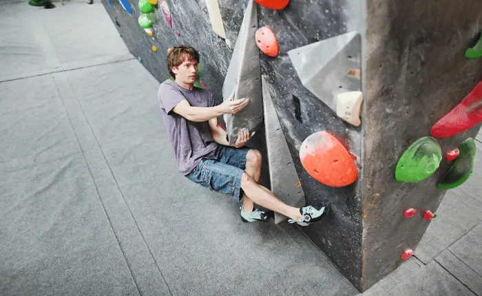 Boy climbing an indoor rock wall with coloured handholds.