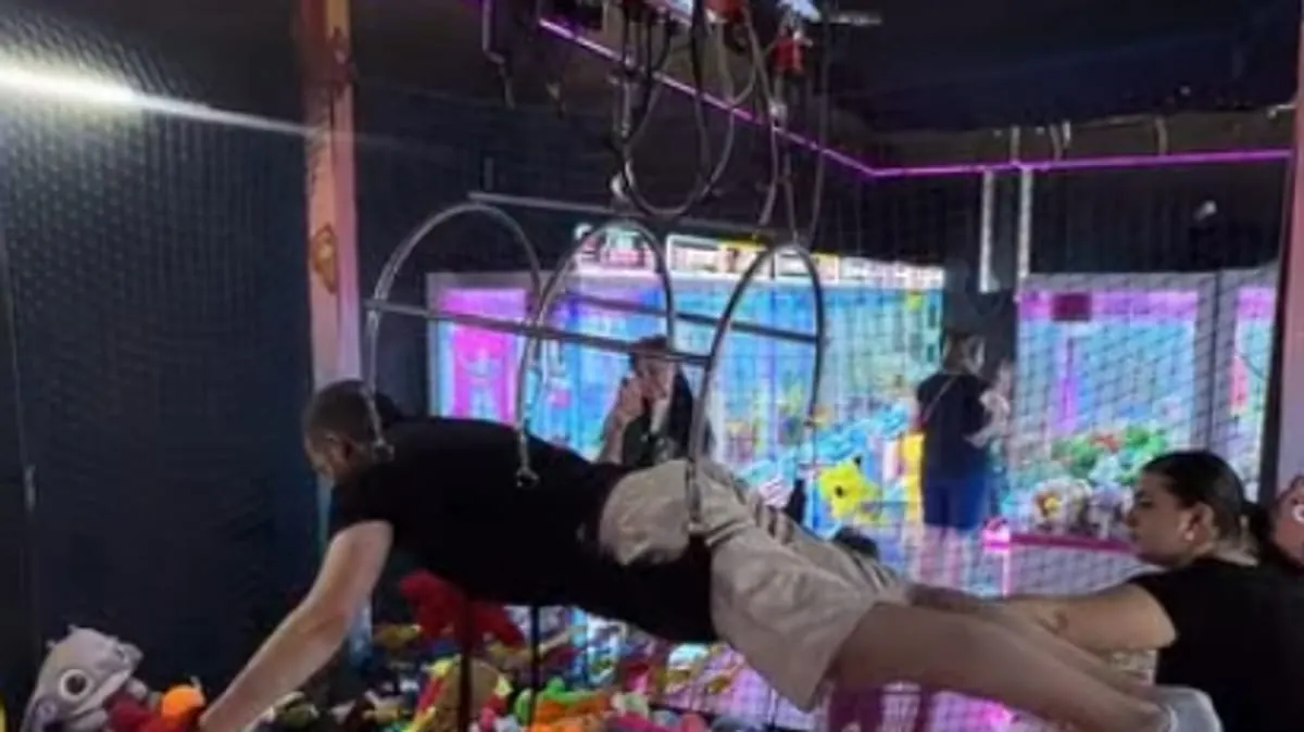Visitors playing at an arcade claw machine game with neon-lit prize displays at night.