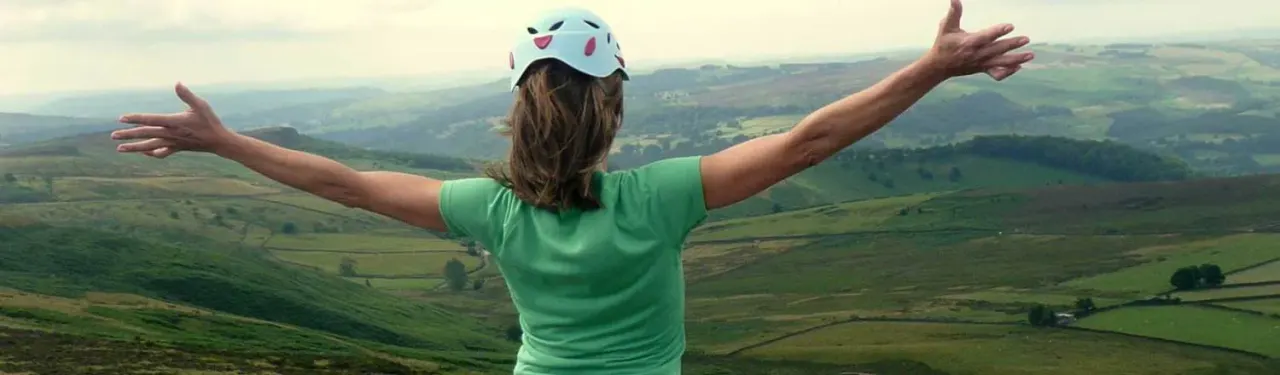 Child wearing a cycle helmet with arms outstretched overlooking rolling countryside hills.