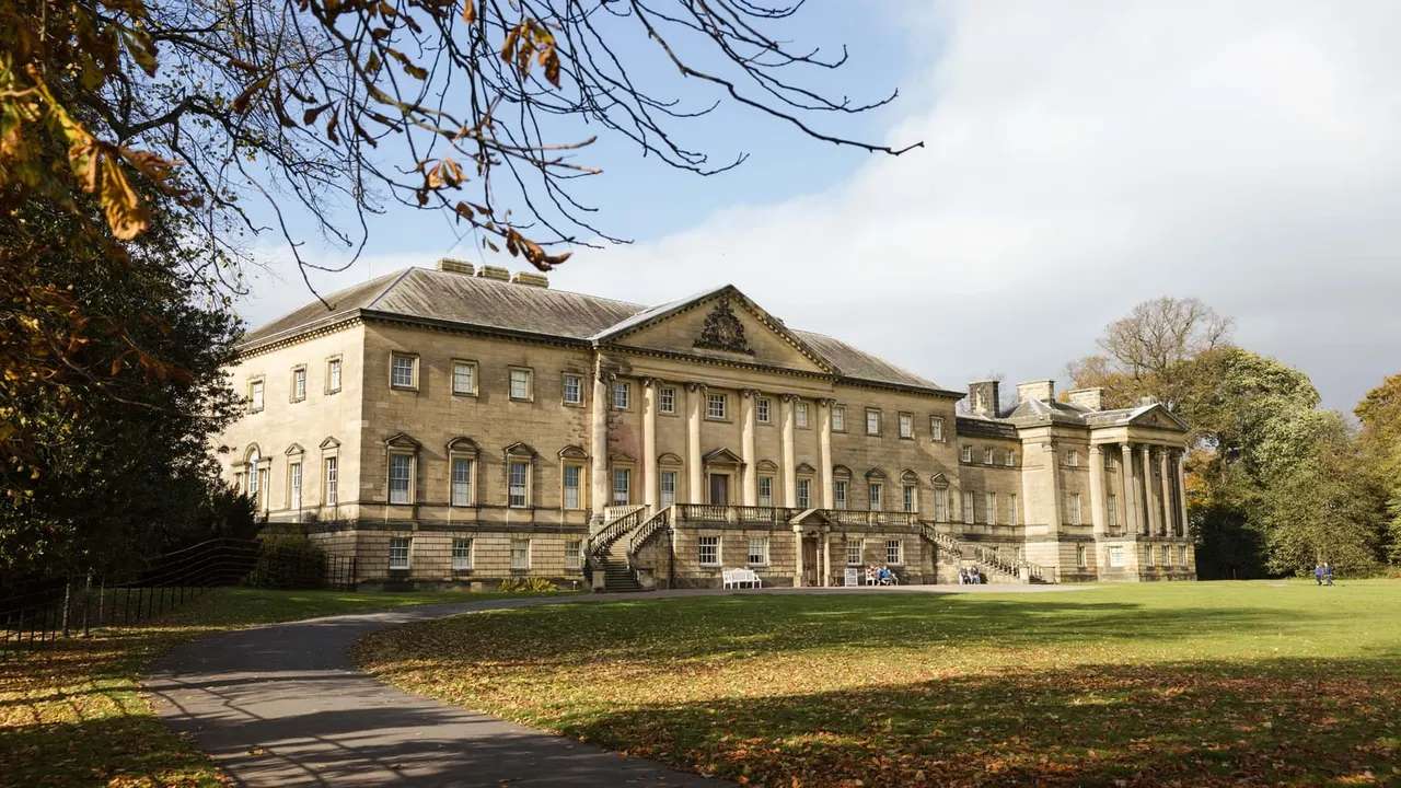 Grand Georgian stone mansion with columned portico set in spacious grounds with autumn trees and lawn.