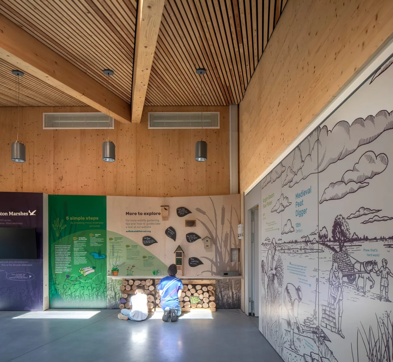 Two children sitting on the floor of a modern wooden interior with educational display panels about wetland habitats and wildlife.