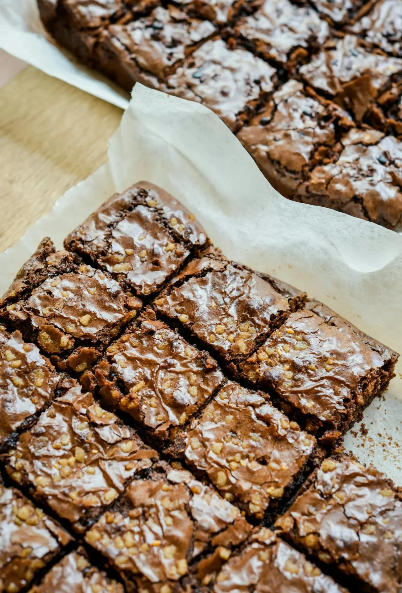 Chocolate brownies dusted with icing sugar, cut into squares and arranged on white paper.