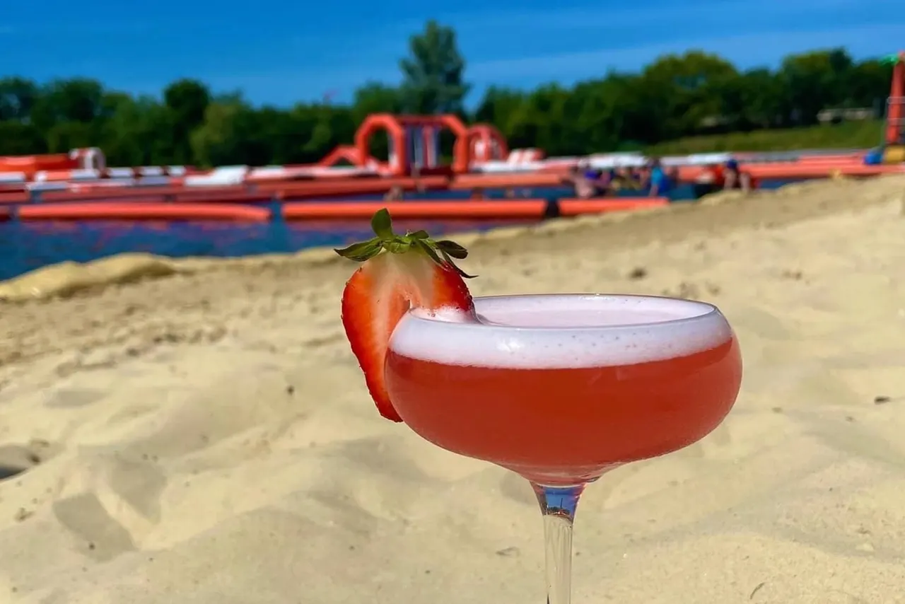 Strawberry cocktail on sand with inflatable obstacle course and trees behind.