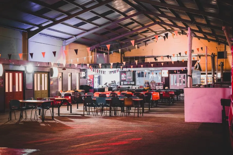 Empty indoor roller skating venue with coloured bunting, tables, chairs and pink wall structures.