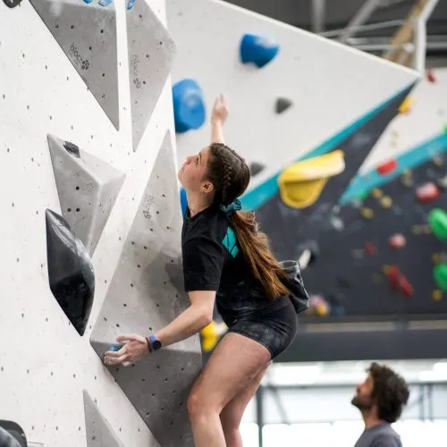 Young person climbing an indoor rock wall with coloured holds at a climbing gym.