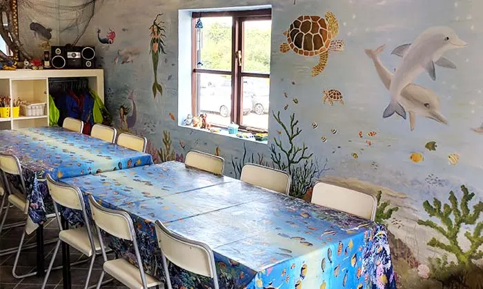 Children's craft room with tables decorated in ocean-themed tablecloths, surrounded by marine wall murals featuring dolphins, turtles and fish.