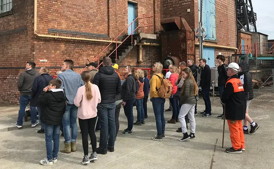 A guided tour group stands in the courtyard of a brick industrial building at a heritage mining site.