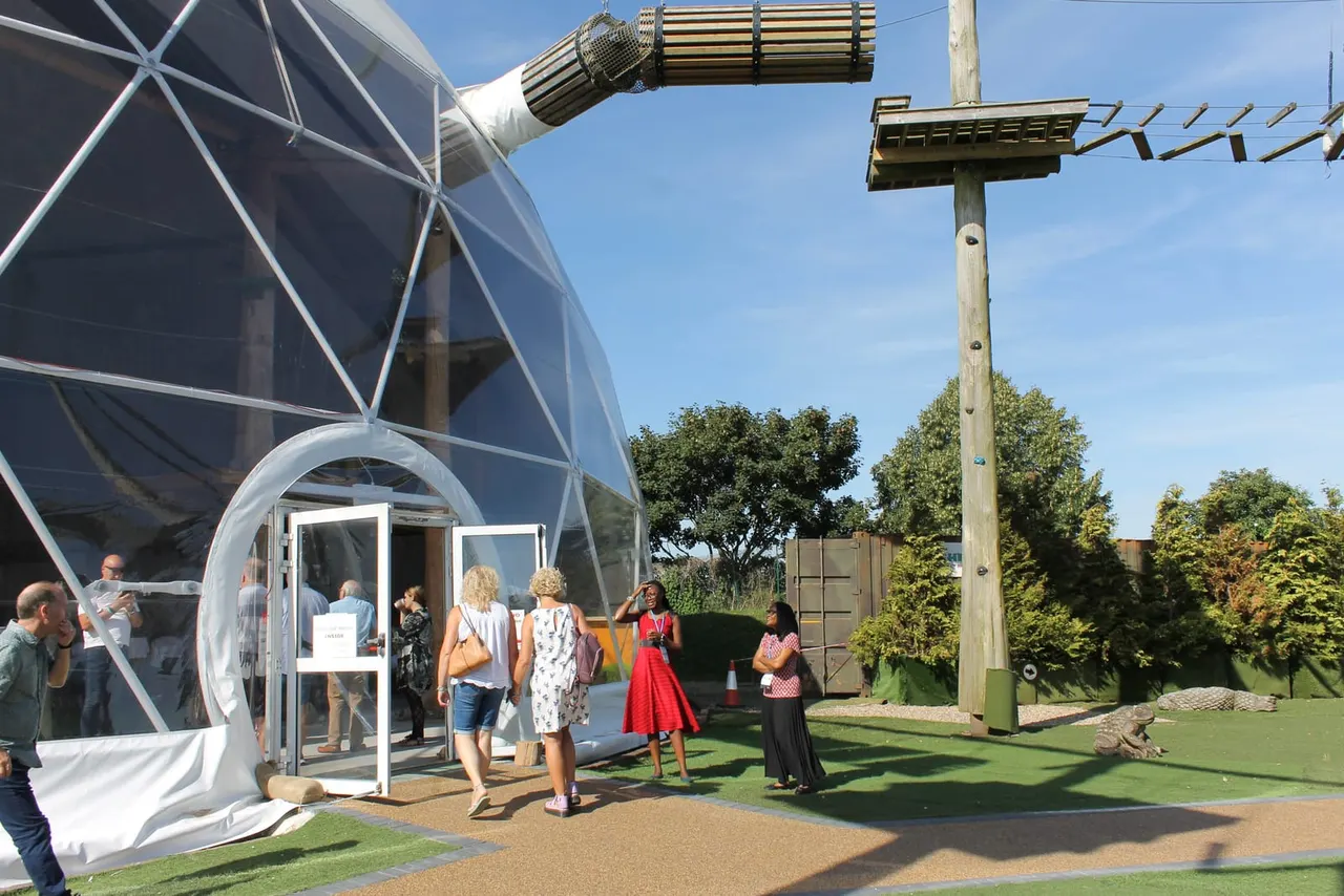 Visitors queuing outside a futuristic geodesic dome structure at an outdoor leisure attraction on a sunny day.