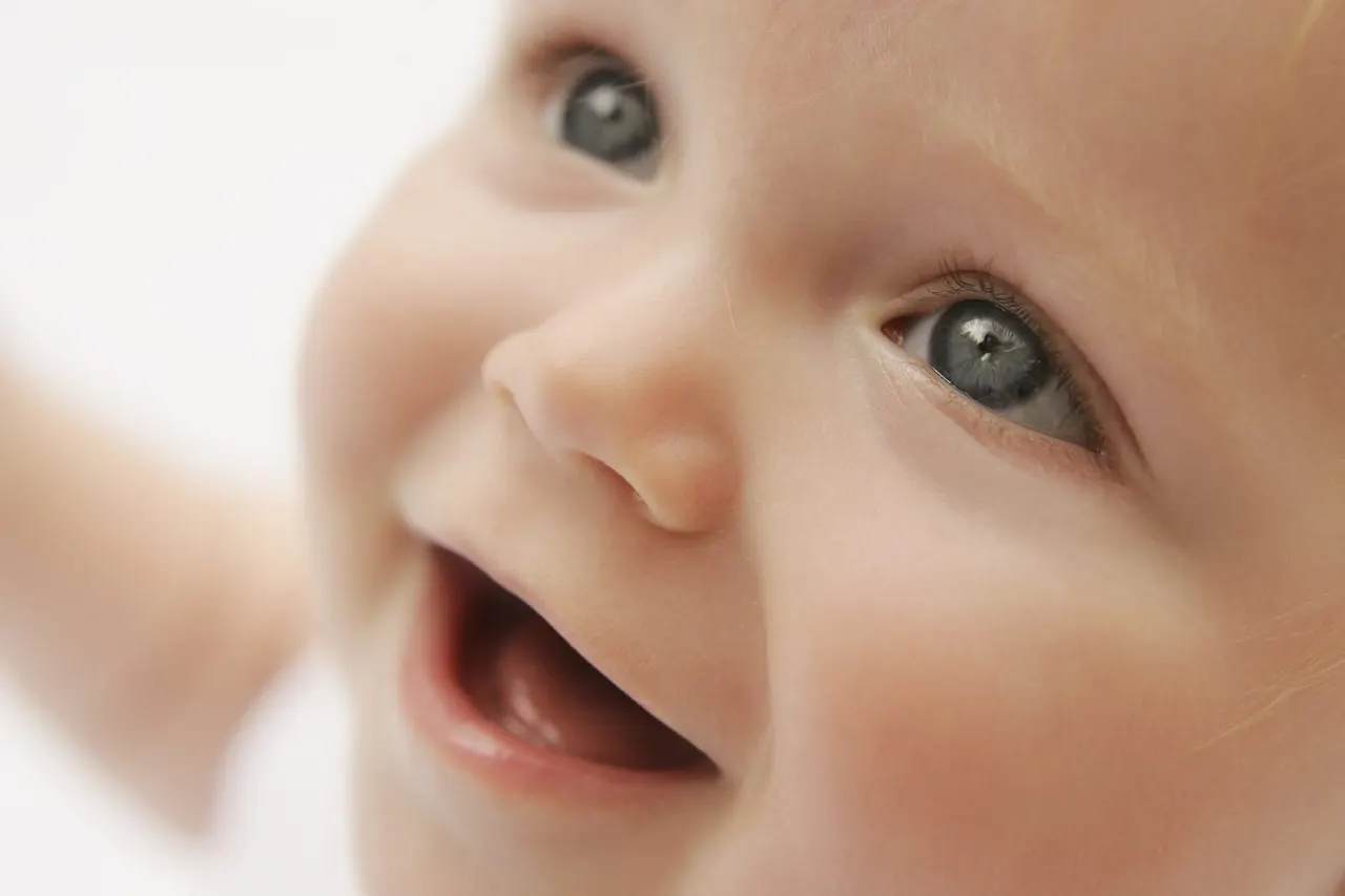 Close-up of a baby's face with wide eyes and open mouth, expressing delight or surprise.