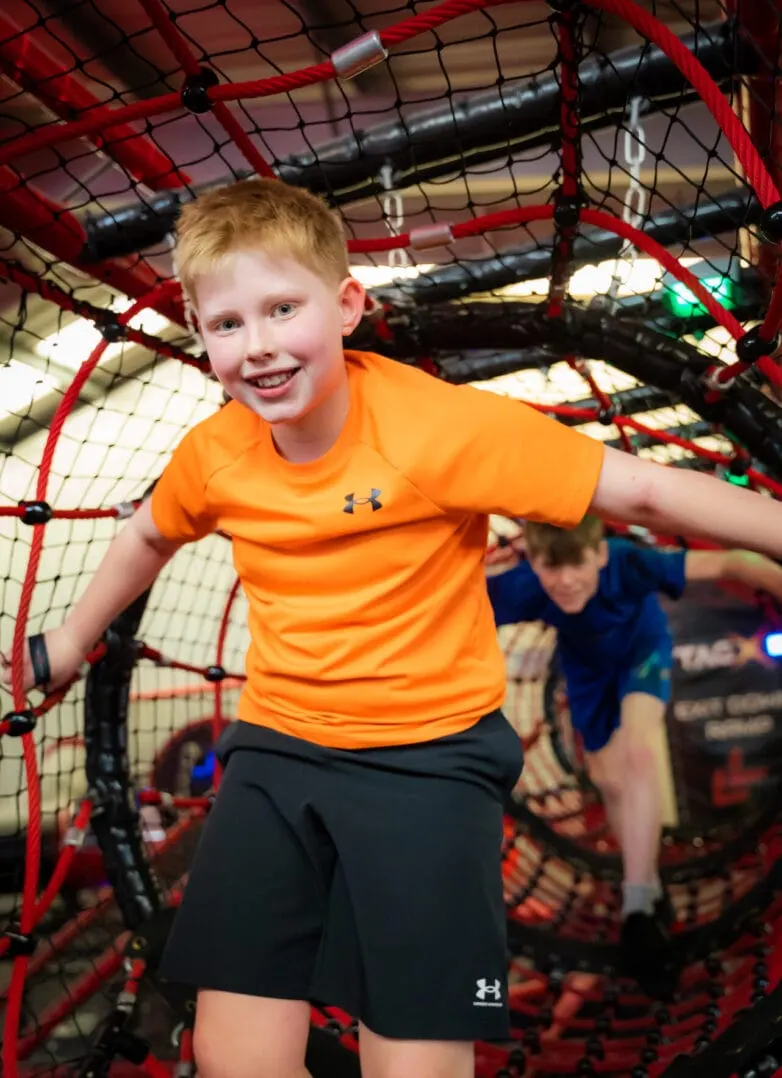 Child in orange shirt playing inside a red and black netted indoor play structure at a leisure facility.