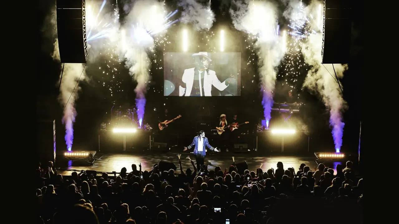 Live concert performance with stage pyrotechnics, a large crowd, and a screen displaying the performer.
