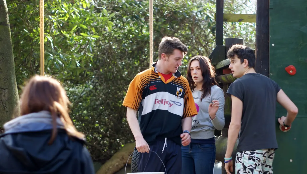 Young people gathering outdoors amongst trees and wooden structures at an adventure activity venue.