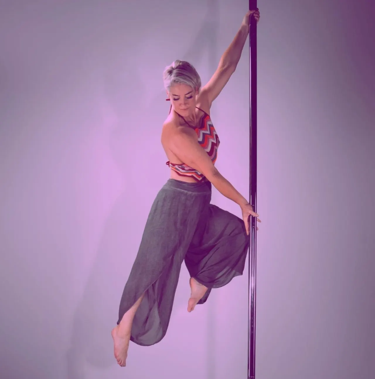 Woman performing an aerial pole dance move against a purple-lit background.