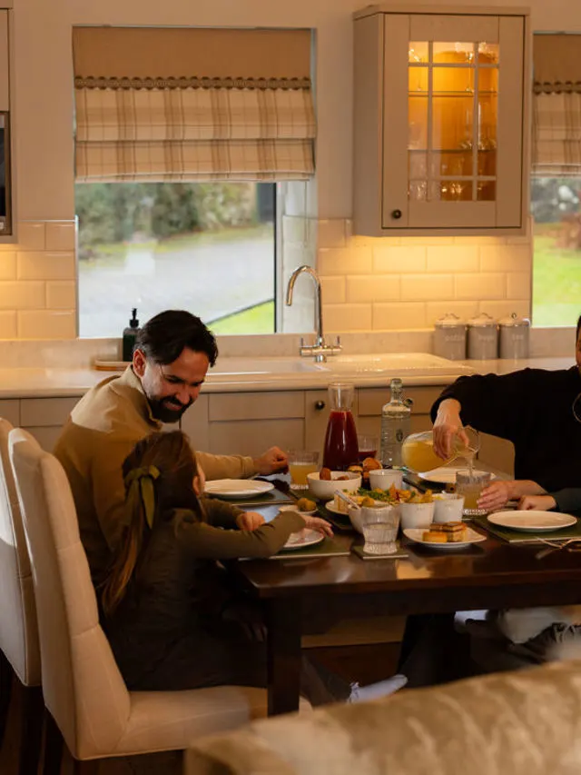 A man and child dining together at a kitchen table with food and drinks, countryside visible through the window behind them.