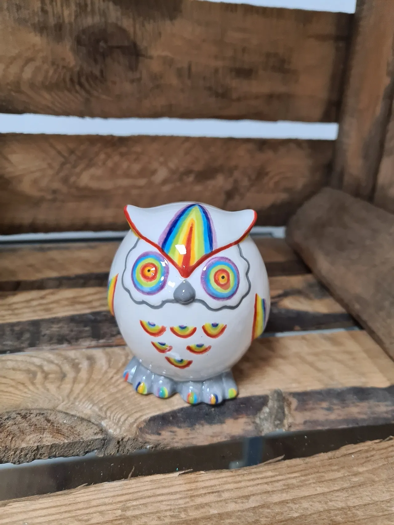 Colourful ceramic owl figurine with rainbow details displayed on rustic wooden beams.