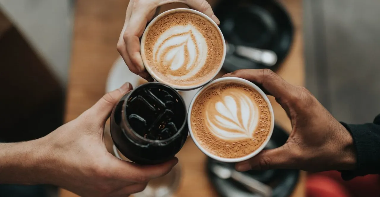 Two people holding three coffee cups with latte art designs.