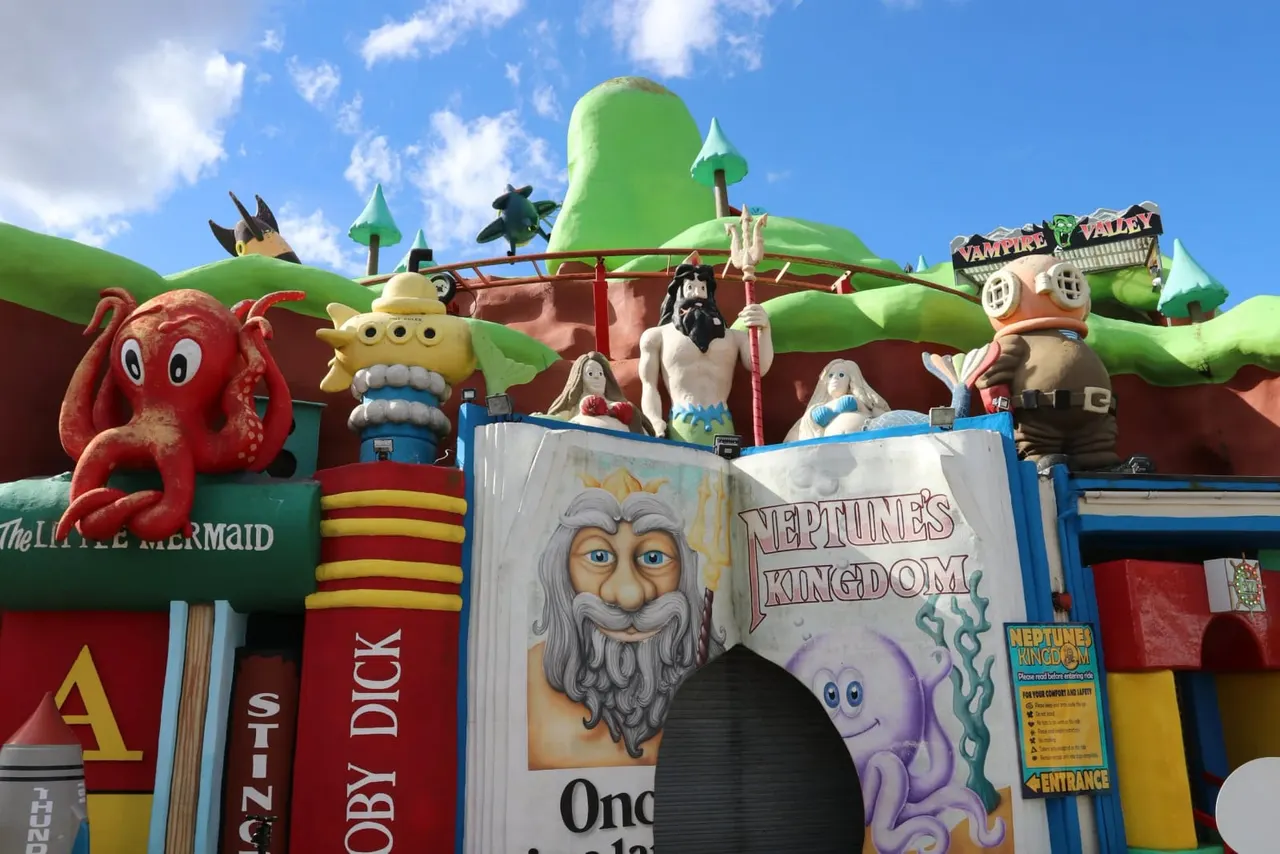 Brightly coloured fairground ride with whimsical themed characters and structures against a blue sky.