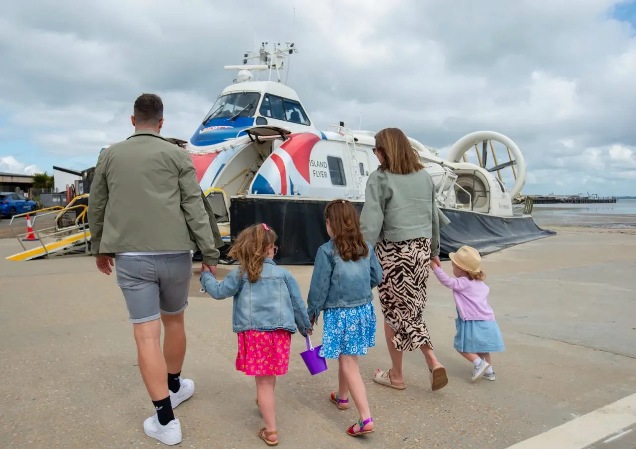 Family walking towards a Union Jack-liveried hovercraft on a beach, ready to board.