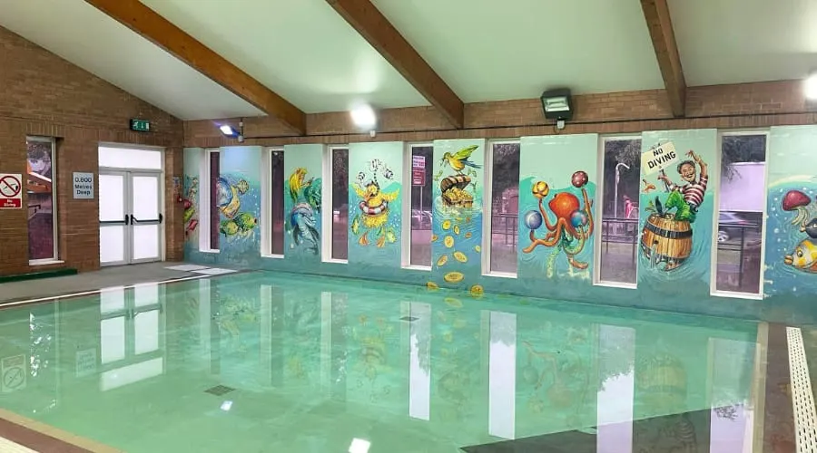 Indoor swimming pool with colourful sea-life murals on the walls and calm turquoise water reflecting the space.