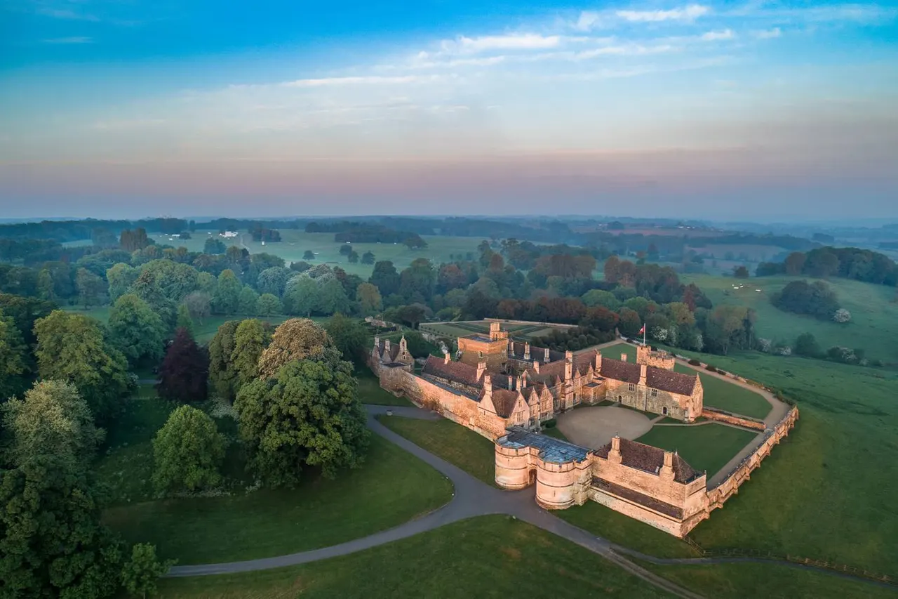 Aerial view of a historic castle with stone walls and towers surrounded by parkland, trees and countryside.