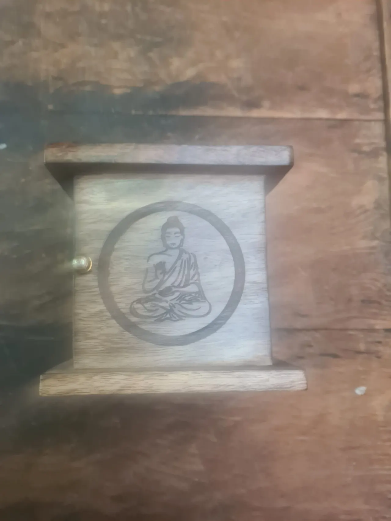 Wooden box with engraved circular design featuring a seated Buddha figure in meditation pose.