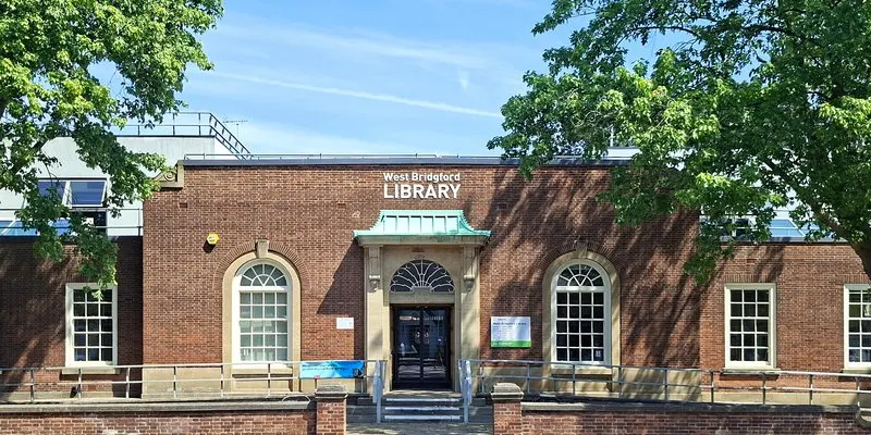 Brick library building with central entrance, stone detailing and fanlight windows under blue sky.