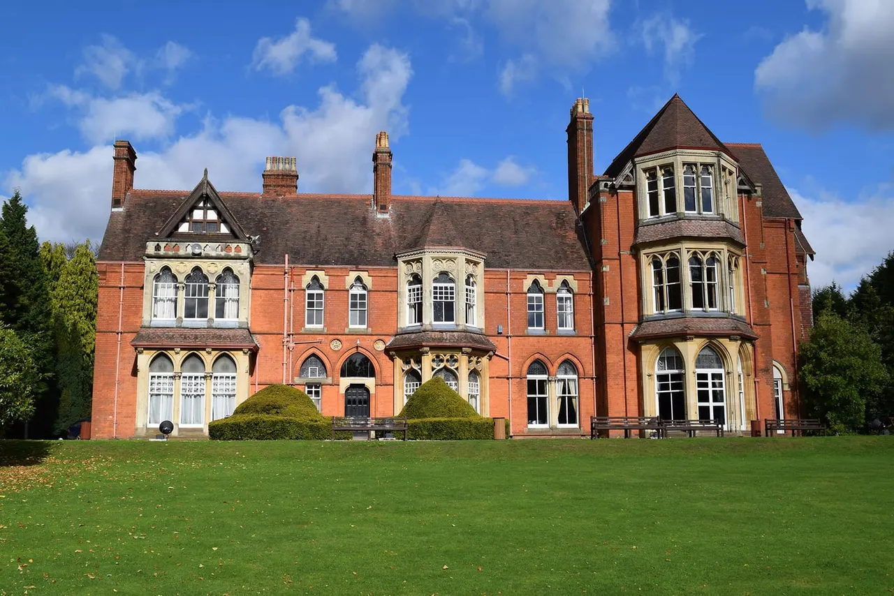 Victorian red brick mansion with decorative stone features and turrets, viewed from across a manicured lawn under blue sky.